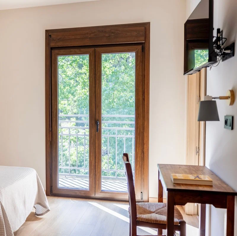 Habitación con puerta de madera y vidrio que da a un balcón con vista a árboles verdes.