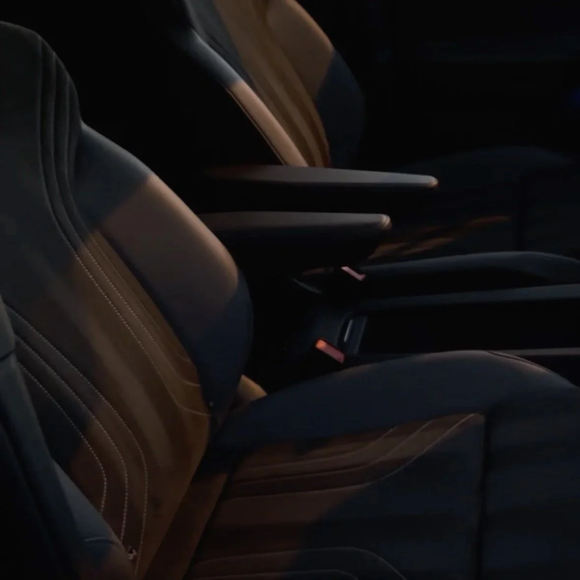 Dark interior seats of a car with black and brown leather upholstery, faintly illuminated in low light.