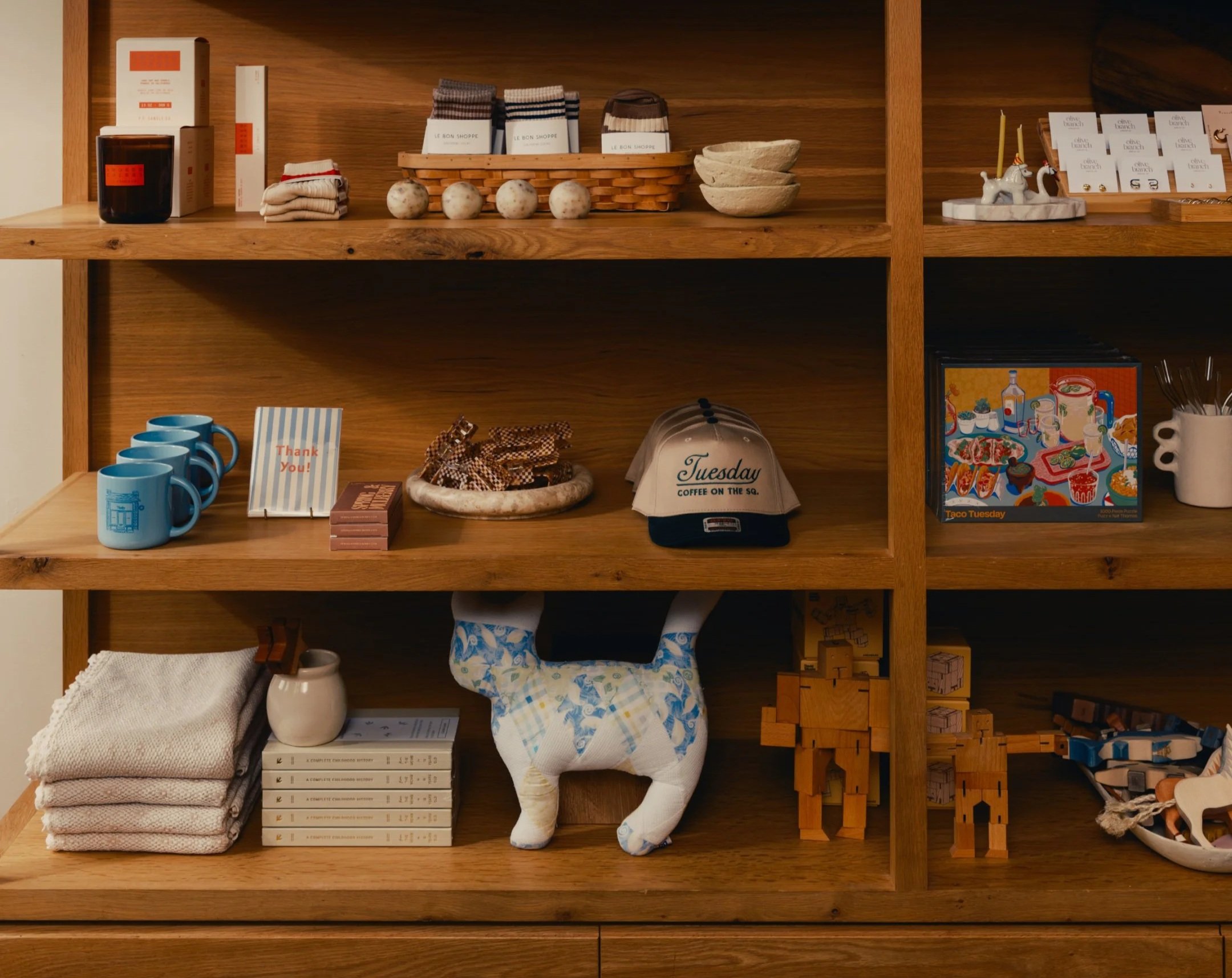 Wooden shelf with various household items including books, mugs, folded towels, ceramic bowls, decorative figurines, and small wooden blocks.