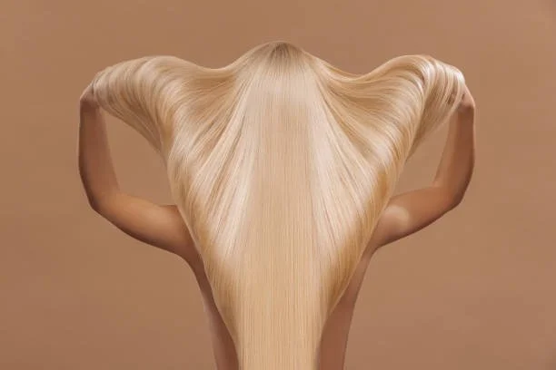 Person with long blonde hair covering their face, arms raised, hair flowing down and curling outward.