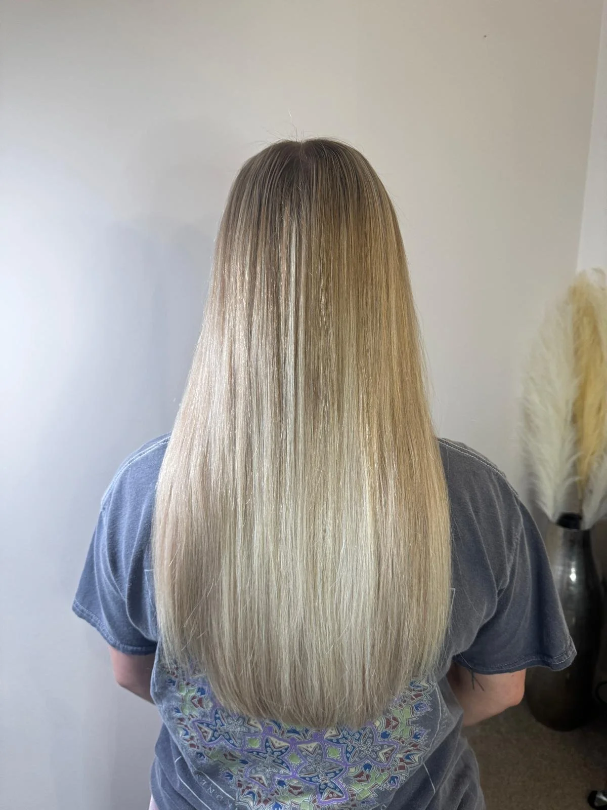 Back view of a person with long, straight blonde hair, wearing a gray shirt.