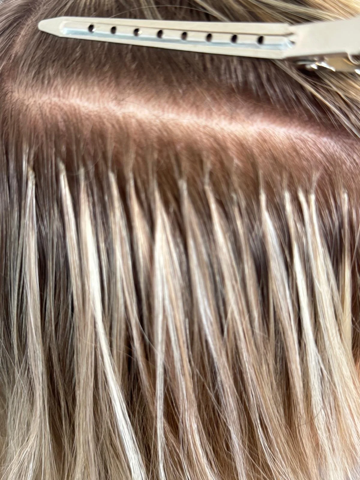 Close-up of a person getting hair extensions or weaves attached, with a hair clip securing hair parted.