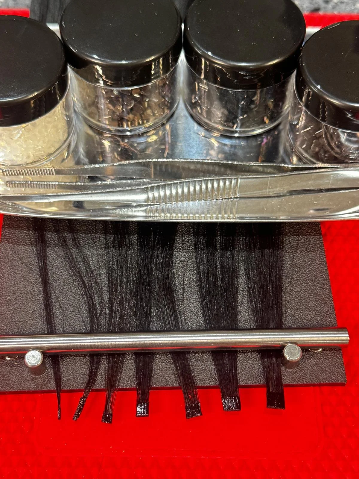 A display of black-tipped hair extensions on a black stand, with small containers of beads and jewelry tools on a tray above, on a red surface.