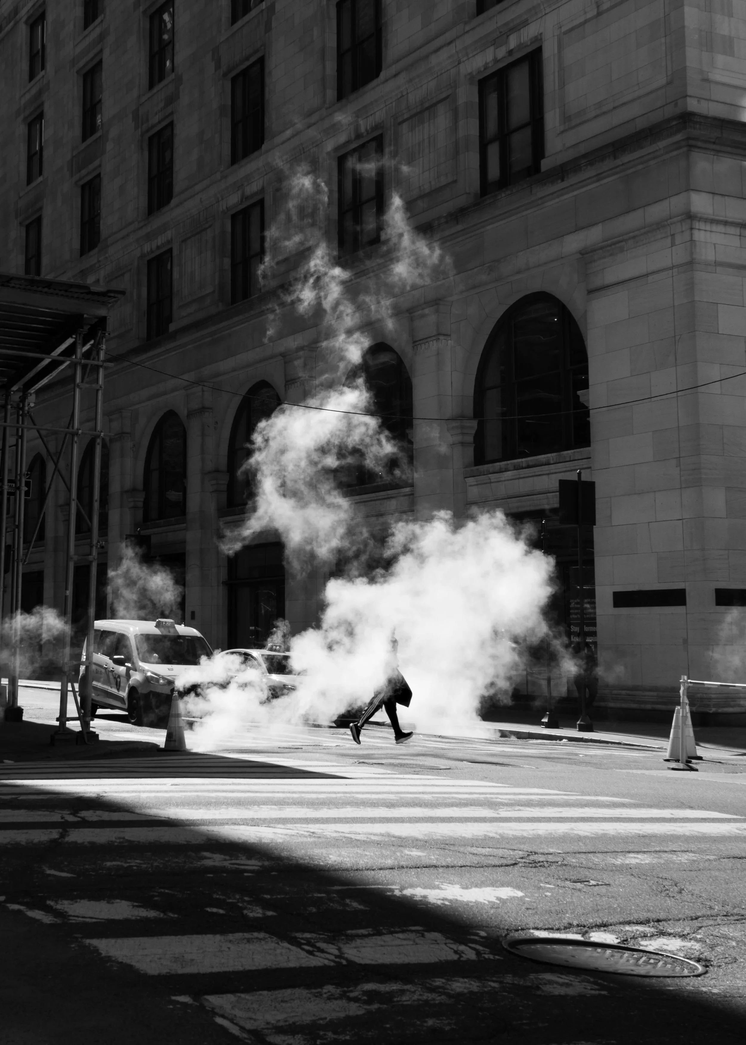 Hot Cross Walk. Black and white photograph of a figure crossing a city street surrounded by steam rising from the ground.