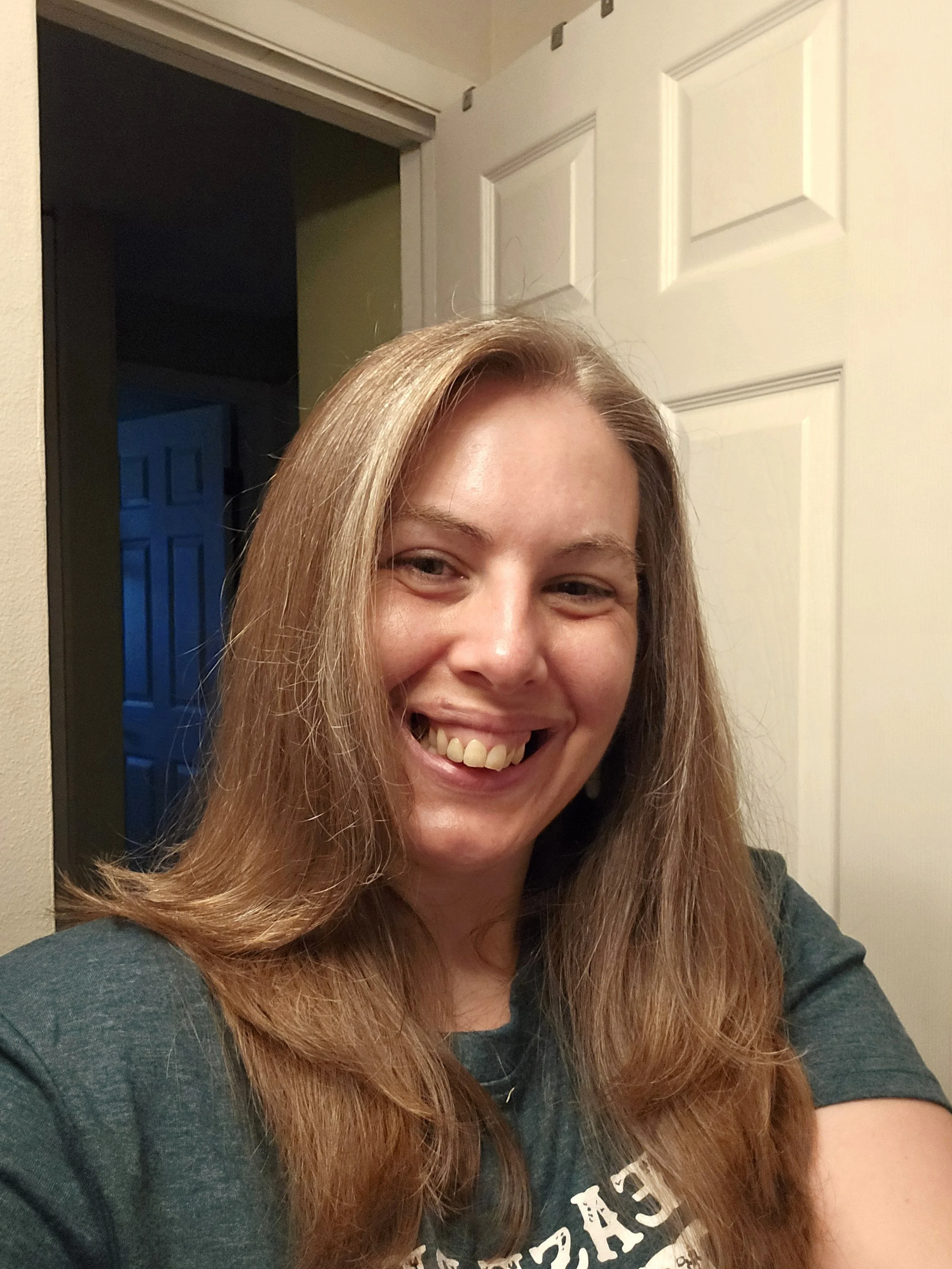 A woman with long light brown hair smiling at the camera in a room with open doorways.