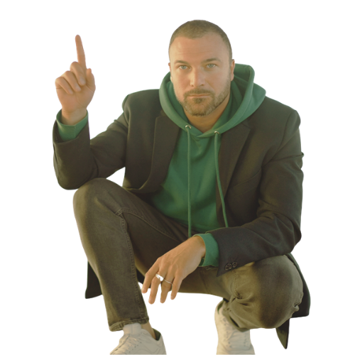 JT Catalano in a green hoodie and black blazer squatting with one finger pointing up, looking directly at the camera.