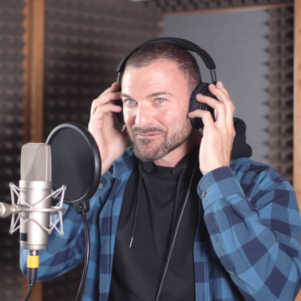 A man in a recording studio wearing headphones, adjusting them while speaking into a microphone.