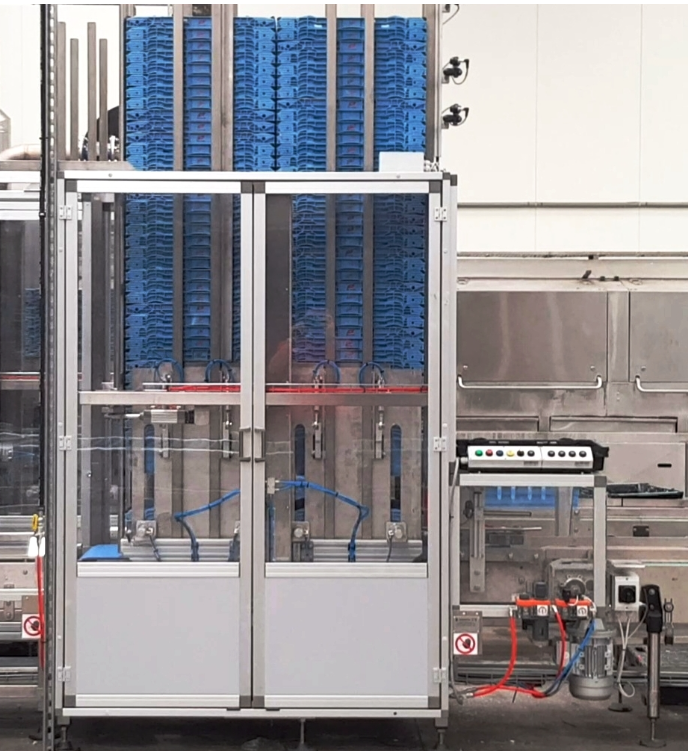 Industrial machinery with blue plastic trays stacked vertically behind glass doors and a control panel on the right.