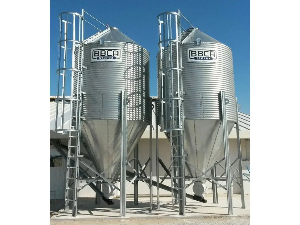 Two large silver metal grain silos with ladders and railings, labeled 'BBCA Storex' on a clear blue sky background.