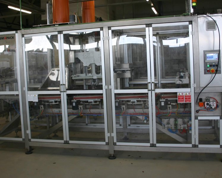 Industrial packaging machine enclosed in transparent safety panels in a factory setting.