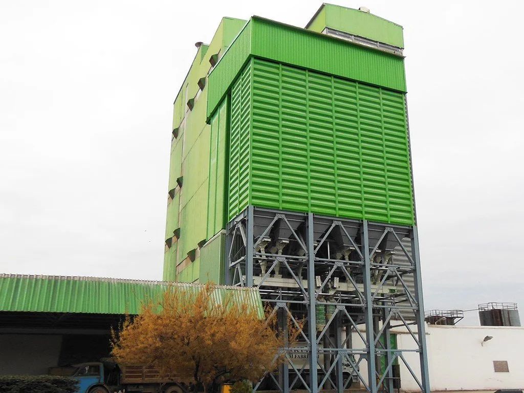 Industrial green building with metal scaffolding, featuring a large green vent or louver structure and a tree in the foreground.