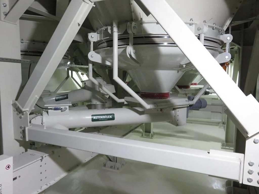 Close-up of a large industrial machine component with white metal framework and pipes, labeled 'ATTINBILEK', situated inside a factory or processing plant.