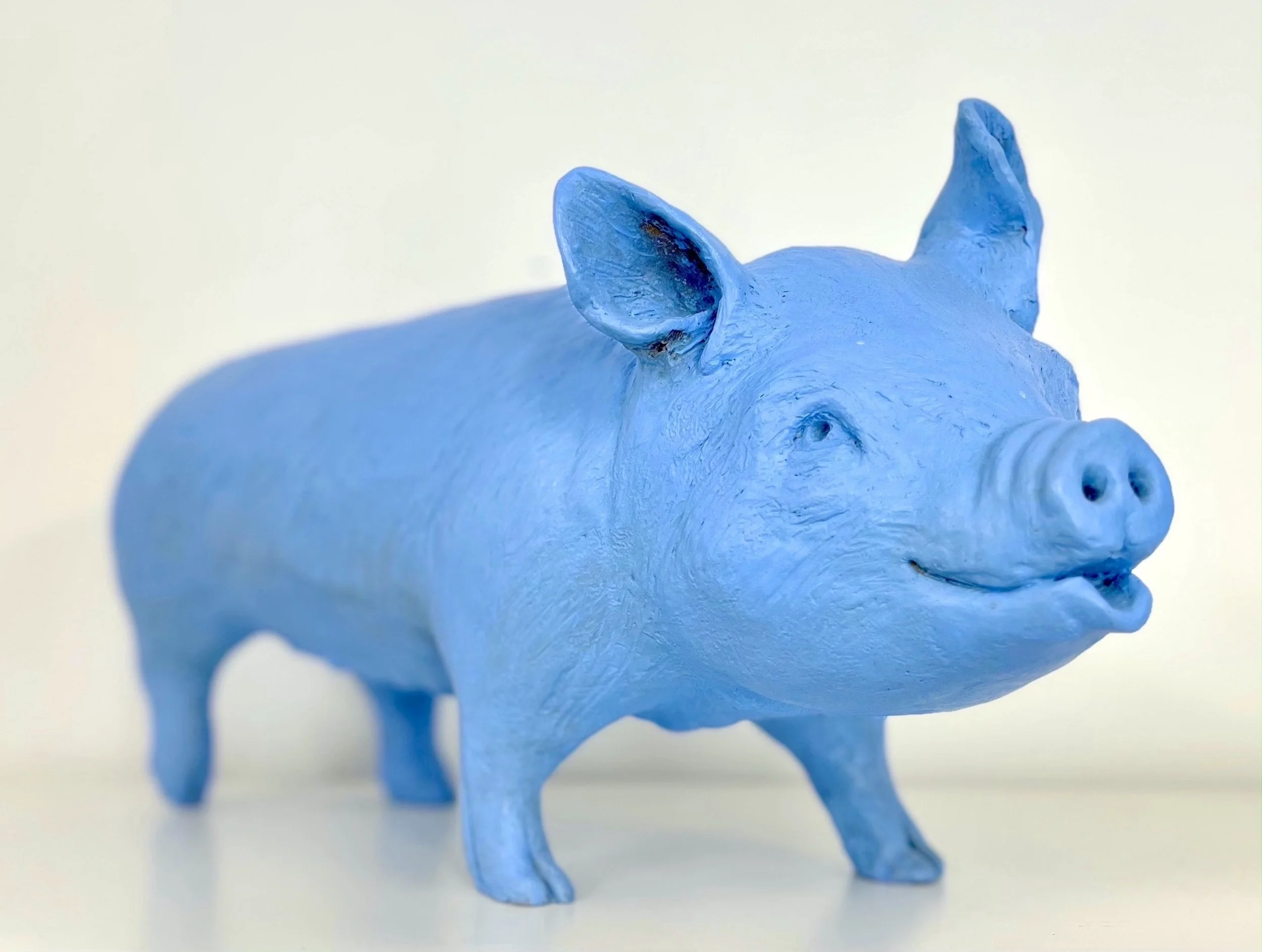 A blue pig figurine with a textured surface and a smiling facial expression