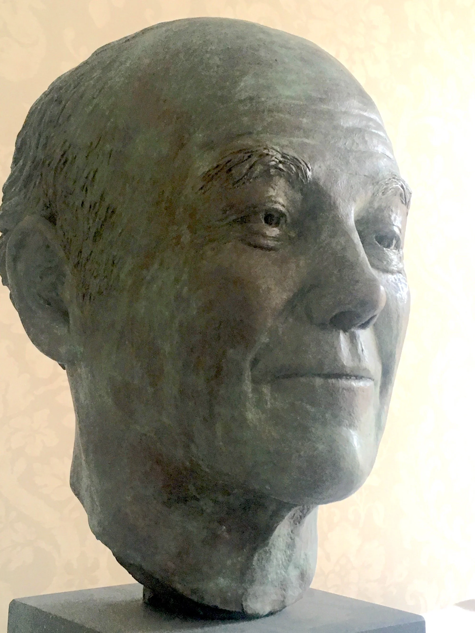 Bronze bust sculpture of an elderly man with a bald head, visible wrinkles, and a serious expression, displayed on a dark pedestal.