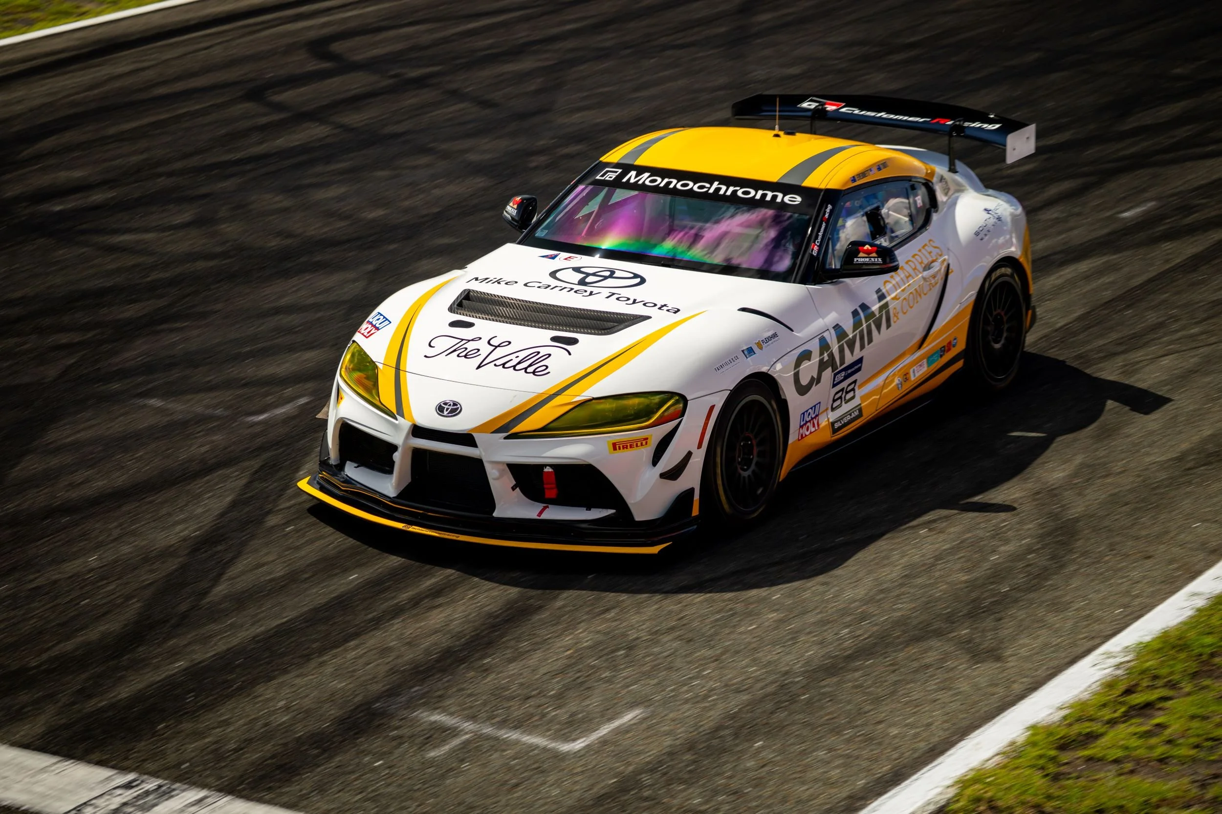 Race car on a track with white, yellow, and black livery, sponsored by Toyota with modem graphics and sponsor logos.