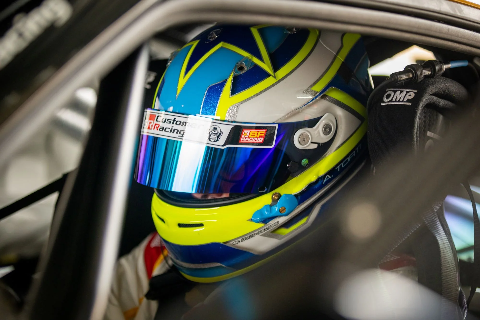 A race car driver wearing a colorful helmet with a reflective visor, inside a race car with safety features.