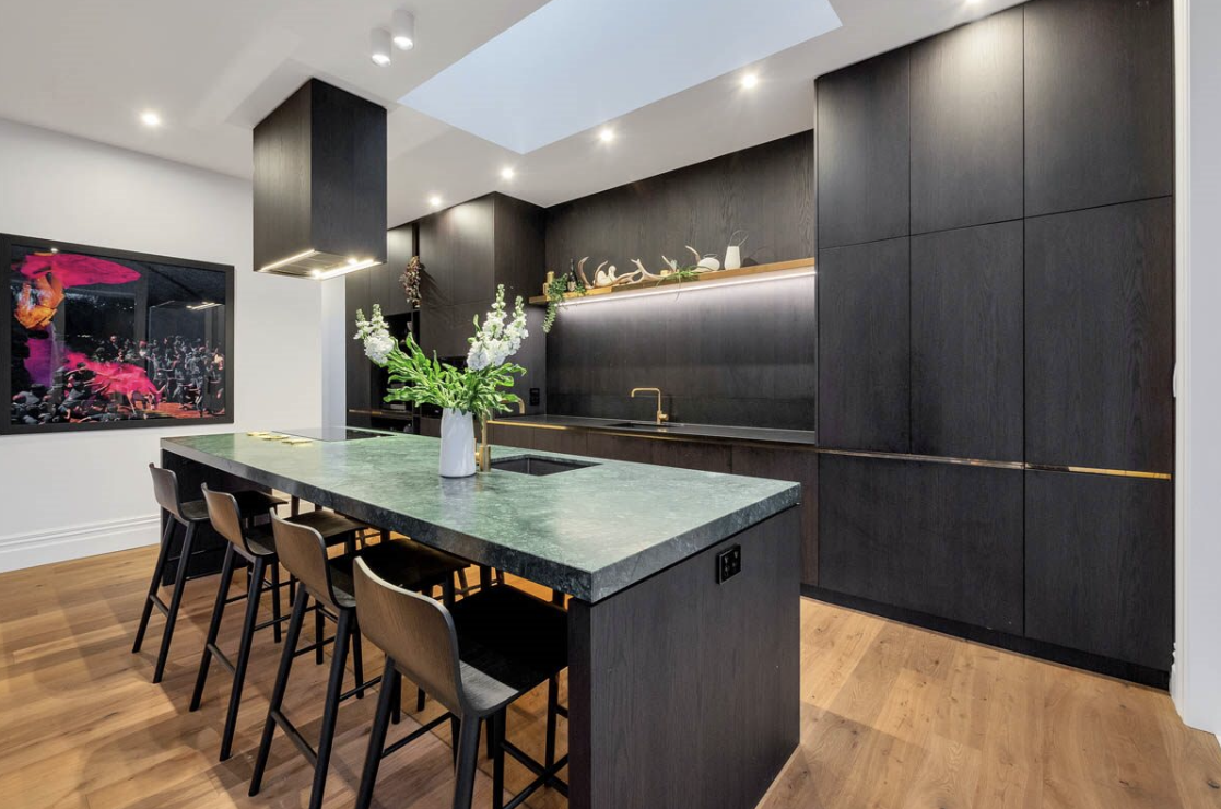 Modern kitchen with dark wood cabinets, a green marble island with a floral vase, and natural wood flooring.