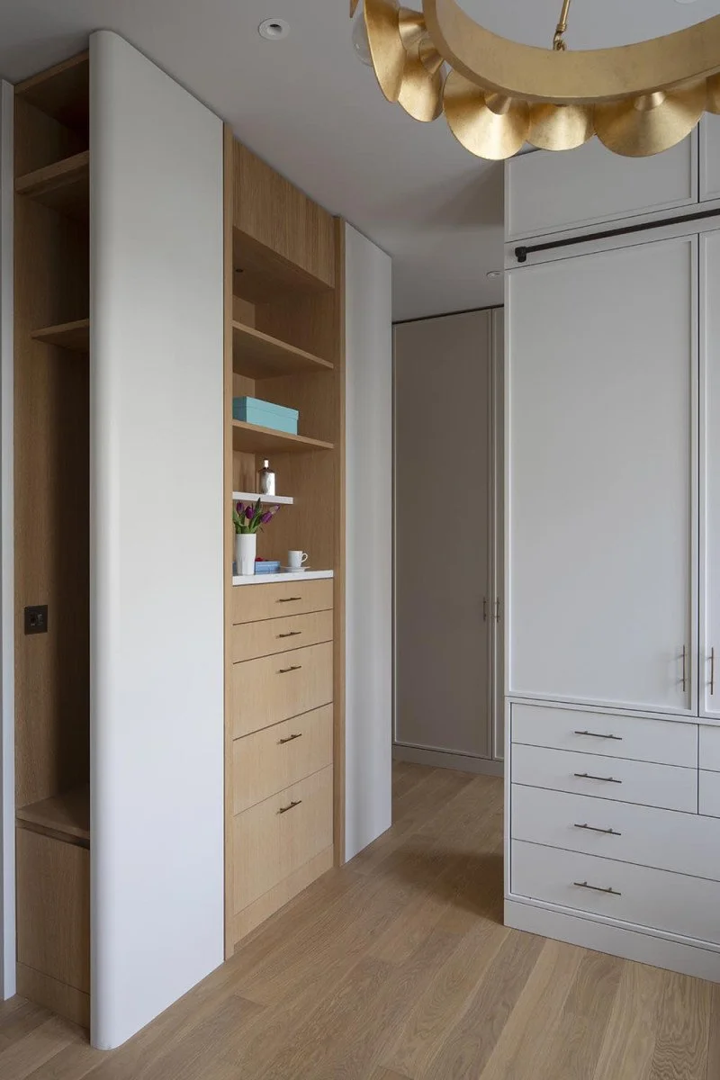 Interior view of a modern room with wood and white built-in cabinetry, a decorative gold ceiling light fixture, and a light wooden floor.