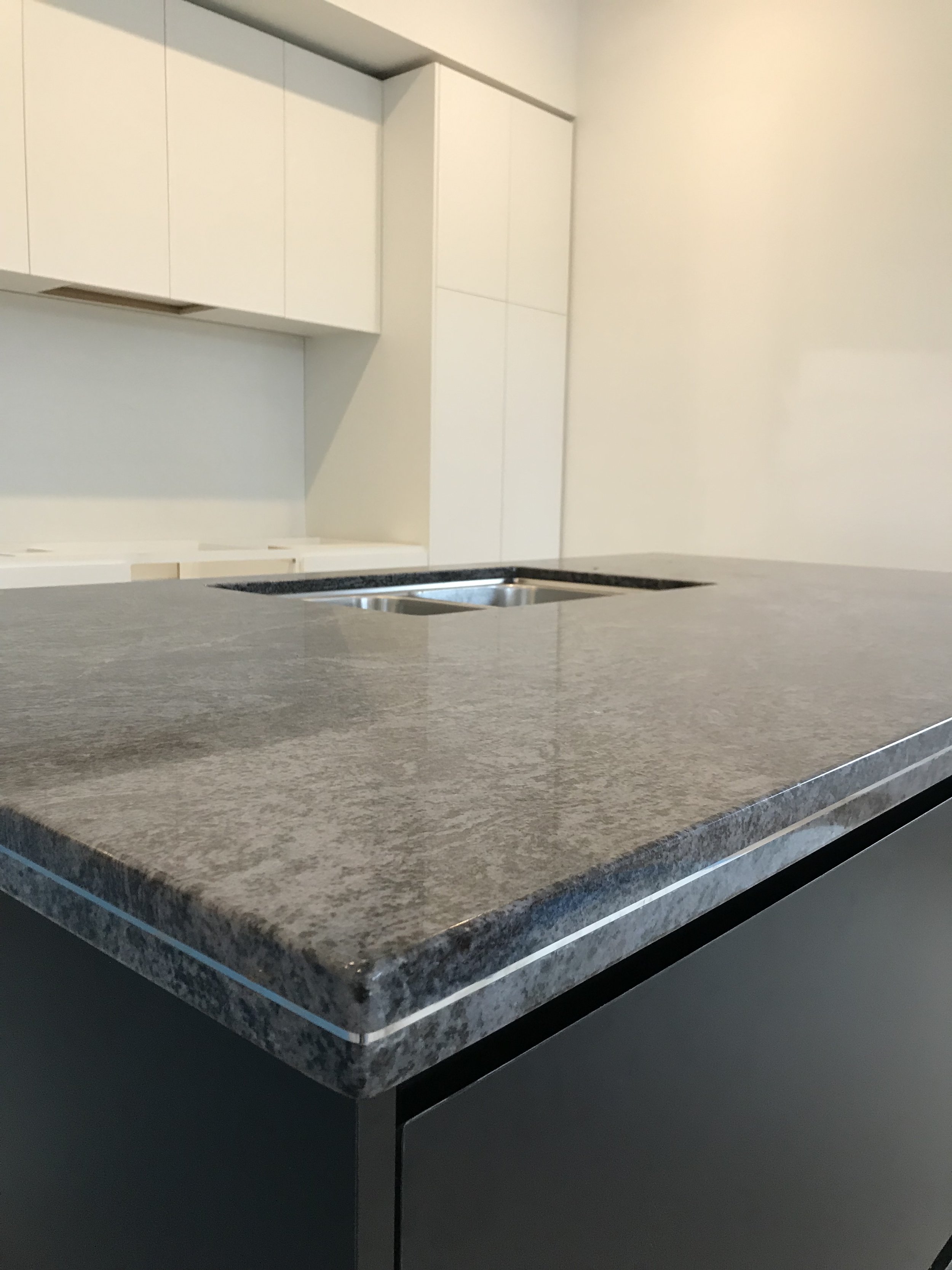 Close-up of a kitchen countertop with a dark stone surface, brownish-gray in color, with a subtle textured pattern.