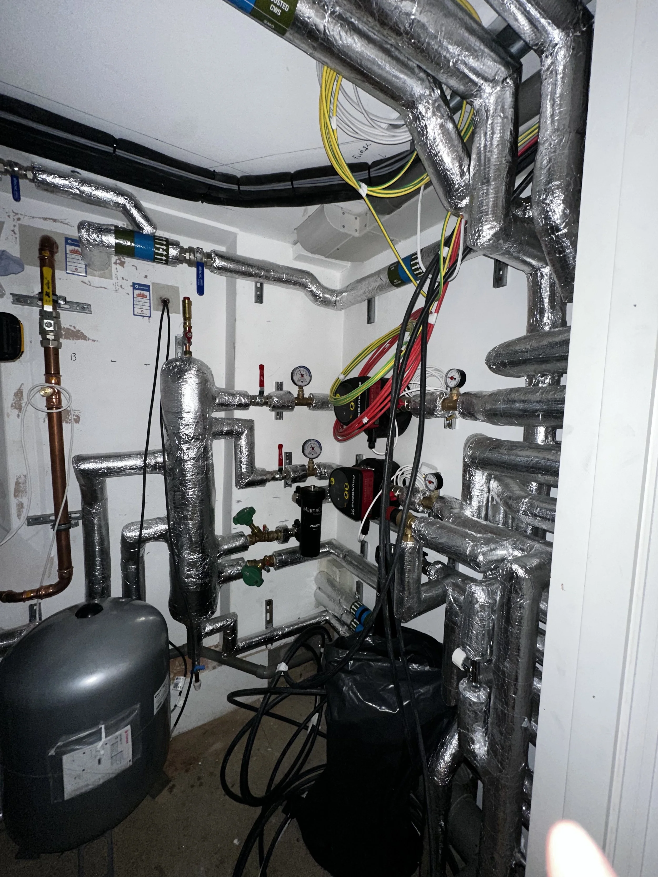 A small utility room with various pipes and gauges, part of a heating or cooling system installation.