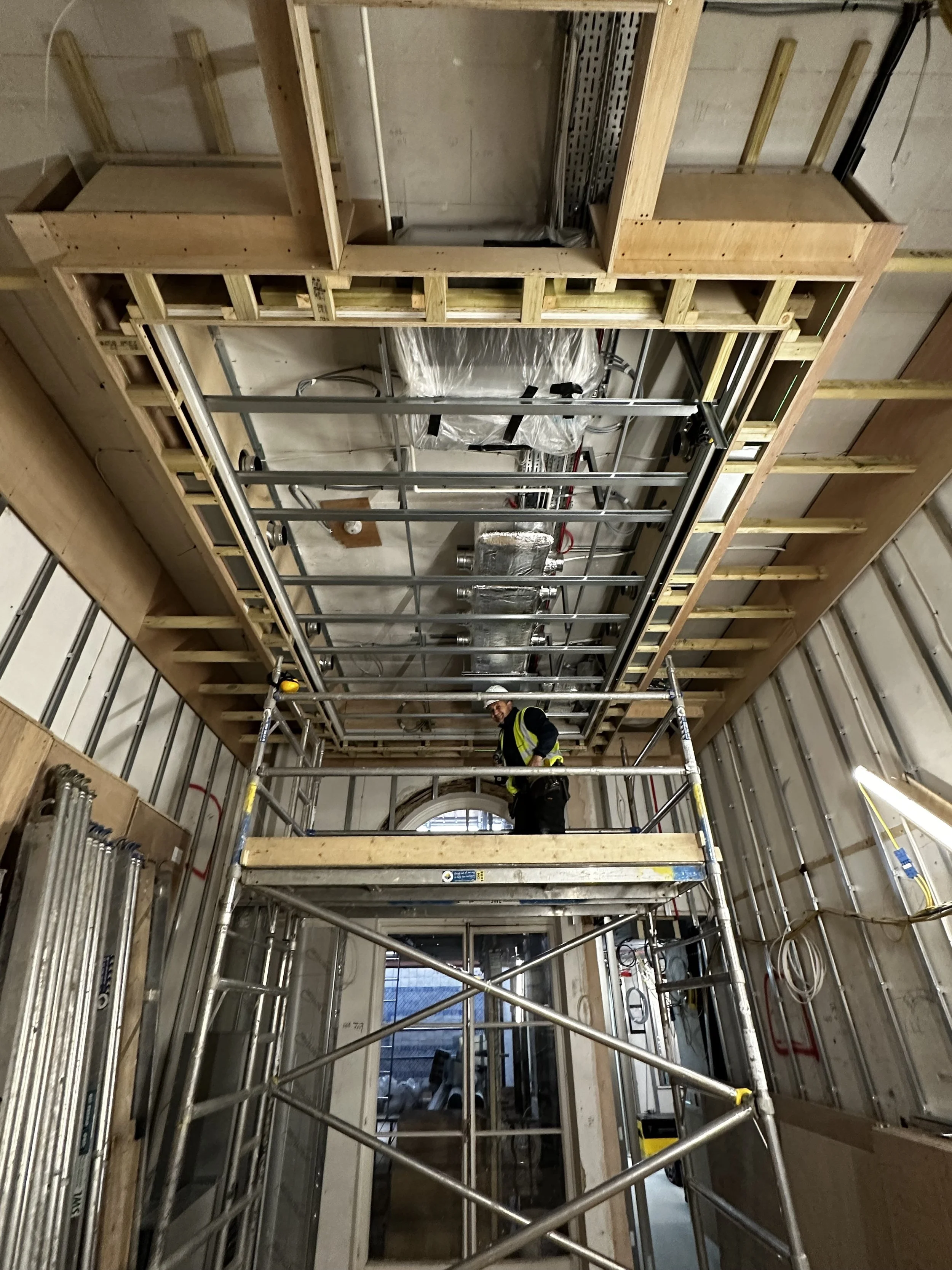 Scaffolding inside a building under construction, with exposed framing, ductwork, and electrical wiring visible.