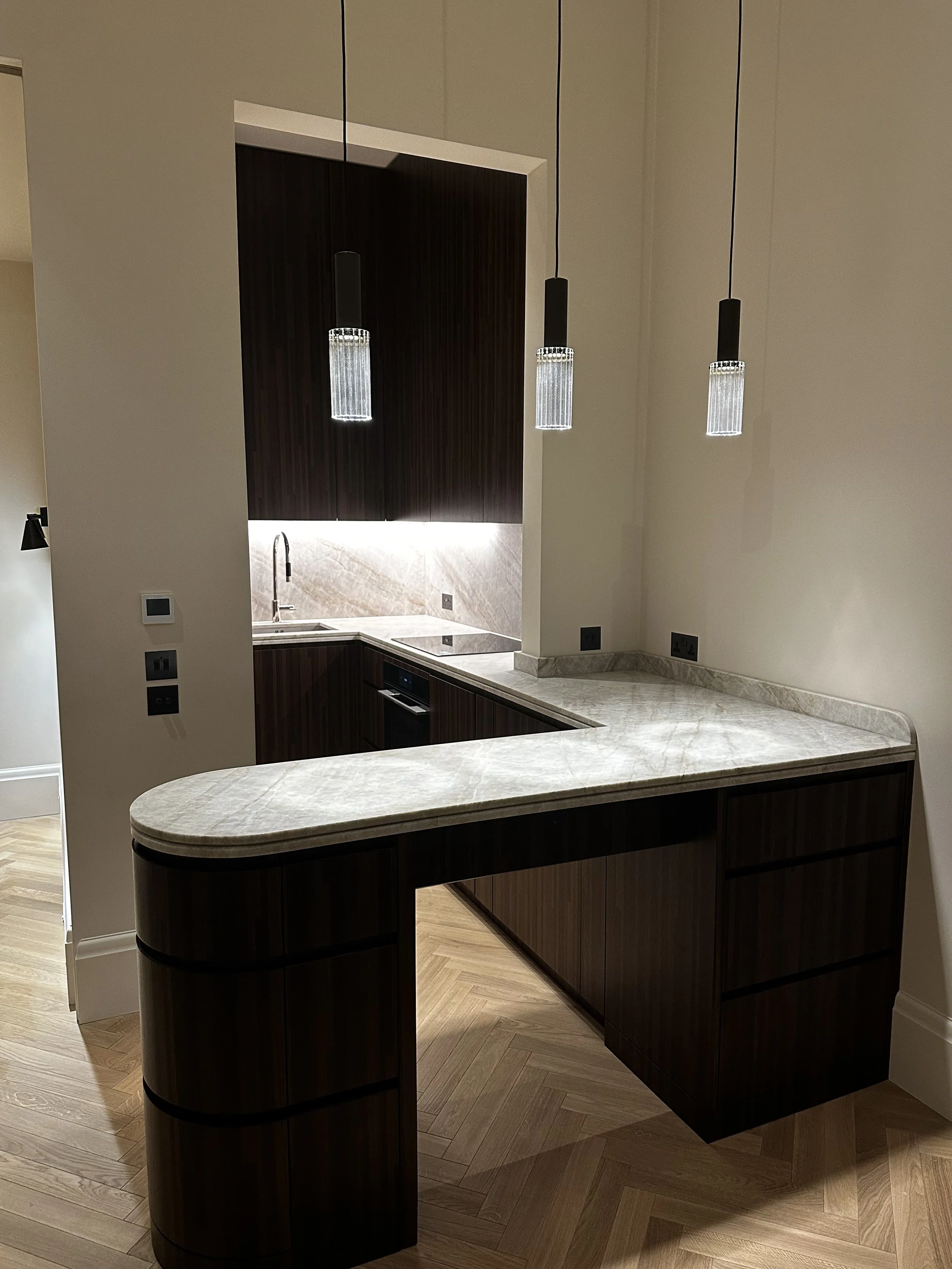 Modern kitchen with dark wood cabinets, marble countertops, a sink, and hanging pendant lights.