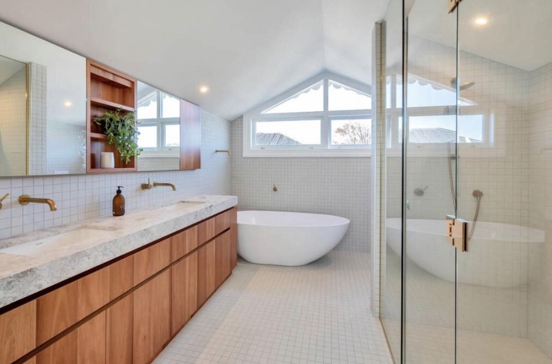 Modern bathroom with a double vanity, wooden cabinets, a white bathtub, a glass-enclosed shower, and windows with a triangular design.