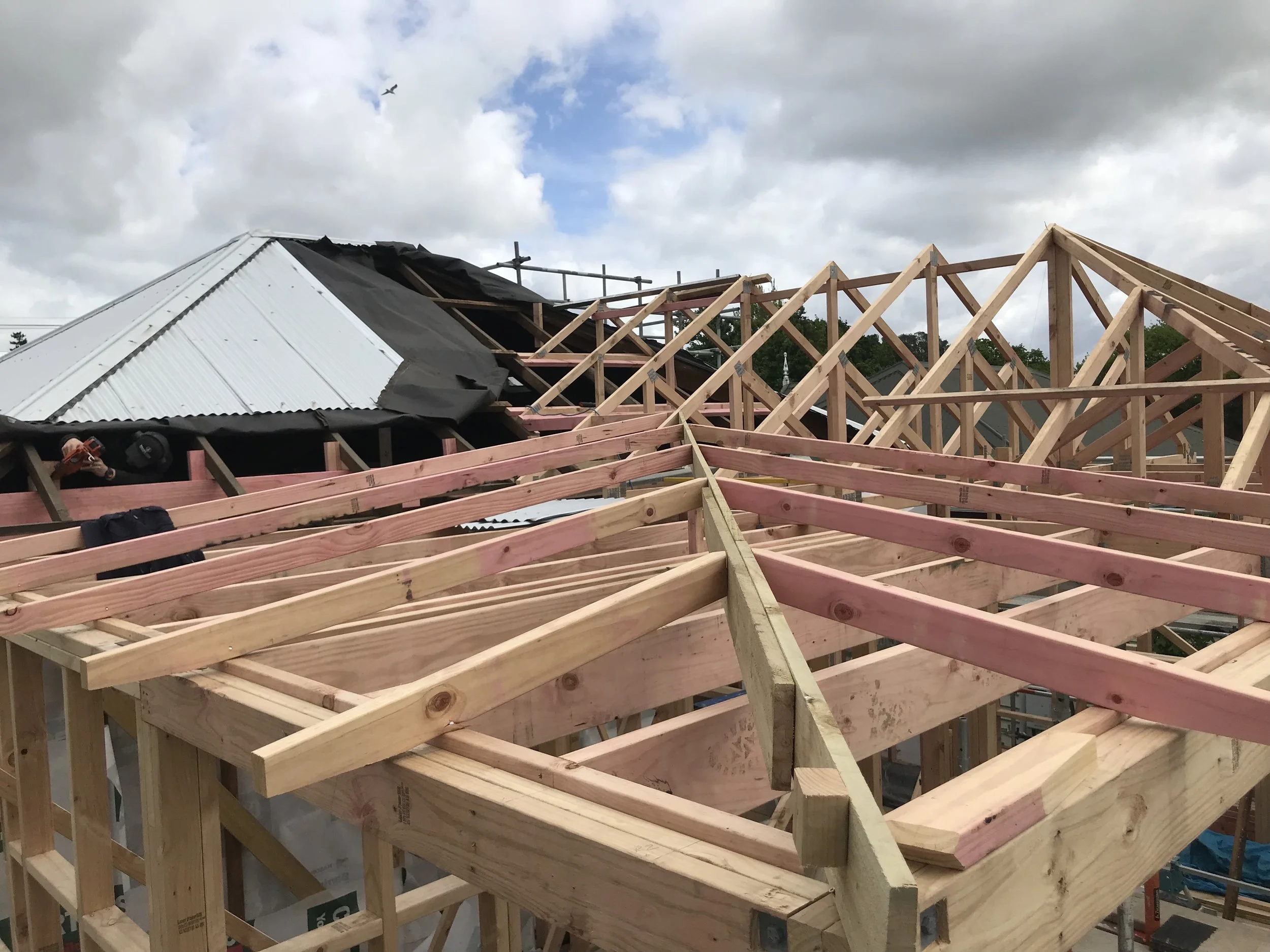 Construction site with wooden roof framework and partially installed metal roofing in cloudy weather.