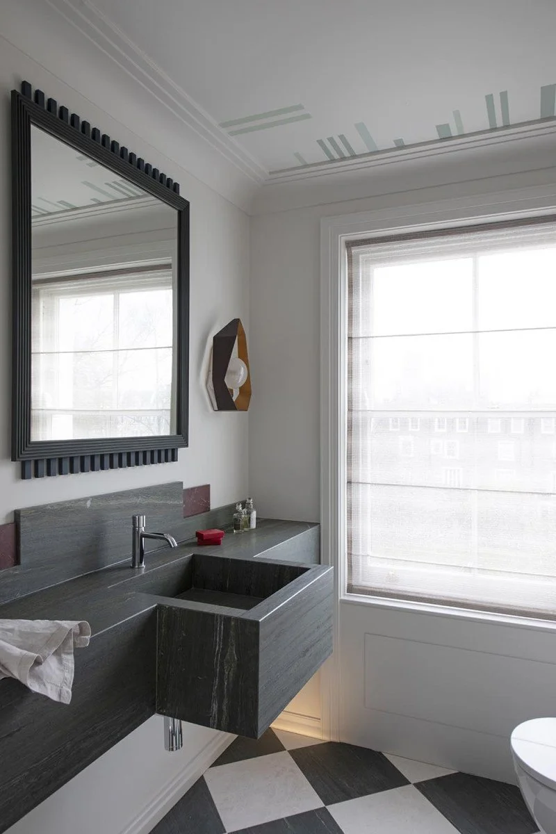 Modern bathroom with a large window, black framed mirror, black stone sink, and checkered black and white floor tiles.