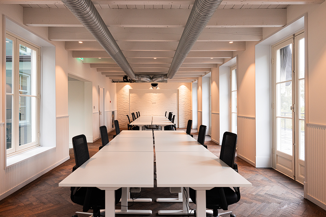 Modern conference room with white tables and black chairs, large windows, and exposed ductwork ceiling.