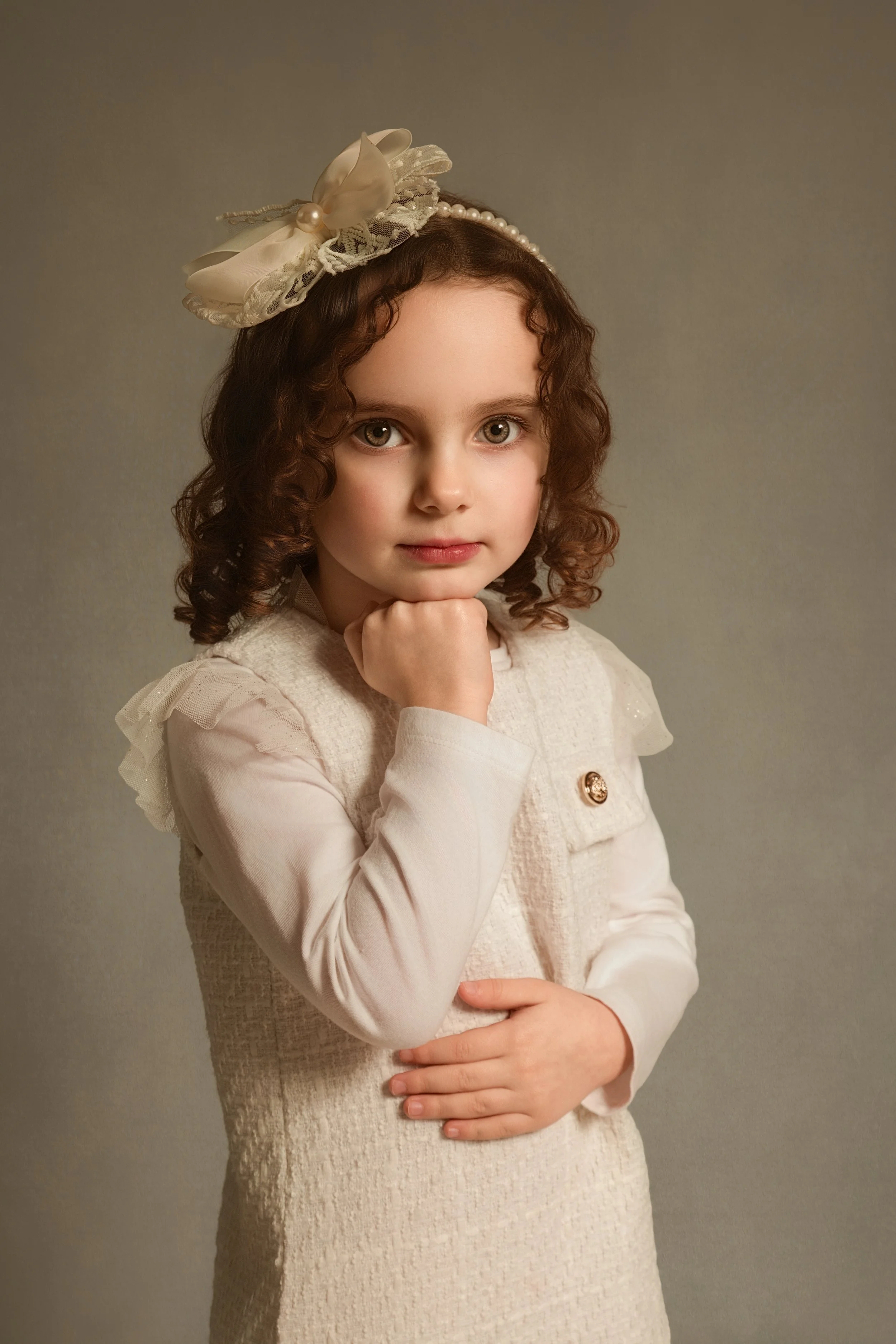 Fine art child's portrait. Brown curly hair and a cream lacy headband with chin resting on her hands by children and family portrait photographer, Bury, Manchester. Photoshoot Lancashire