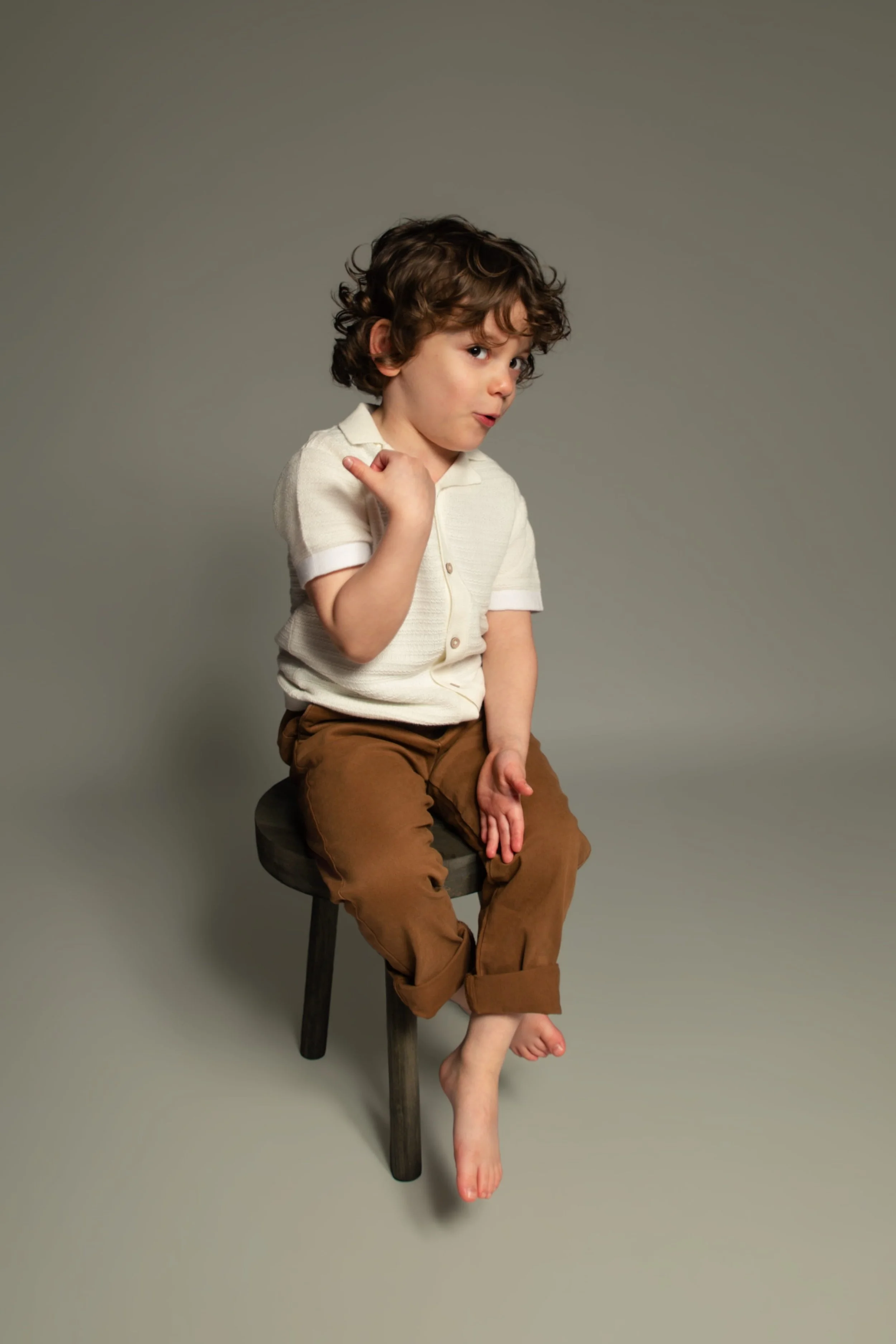 Natural at-home portrait of young boy sitting on a stool and smiling, captured in a relaxed home environment.