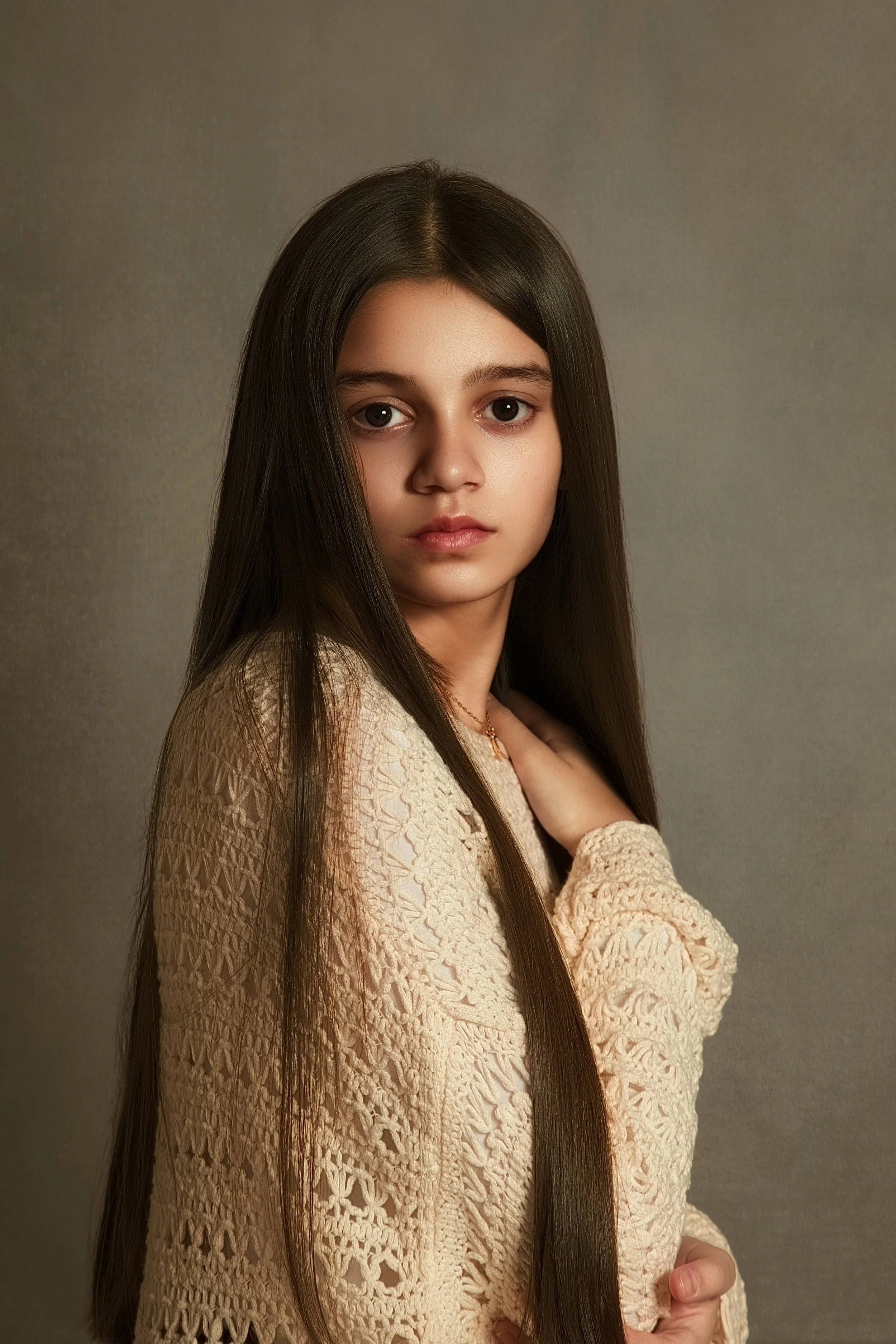 Child fine art portrait photograph. mutes, natural tones, looking directly at the camara. Young teenage girl with long brown haor and a cream crochet jumper