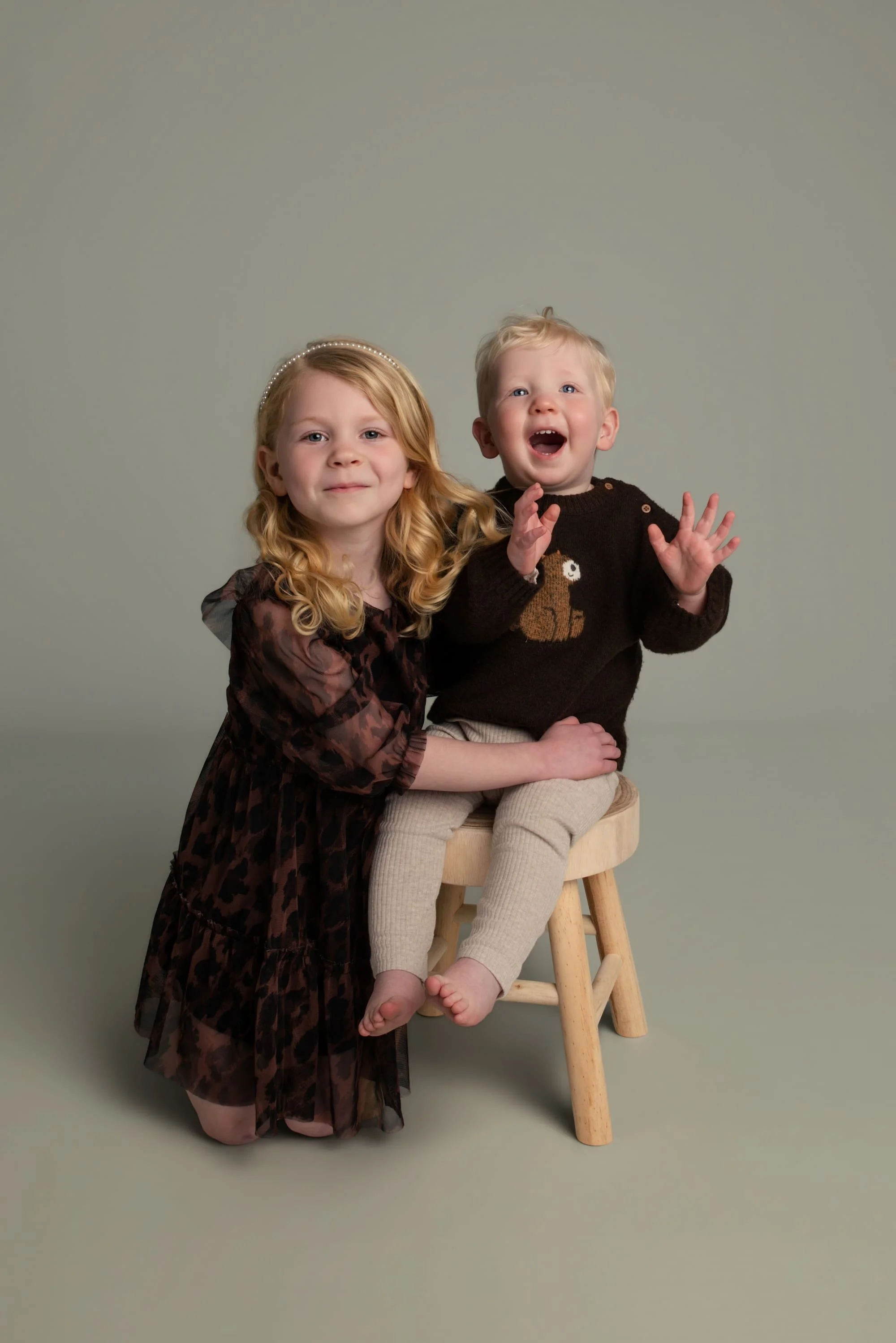 Natural at-home sibling portrait of young girl and toddler boy sitting together on a stool, capturing a relaxed family moment.