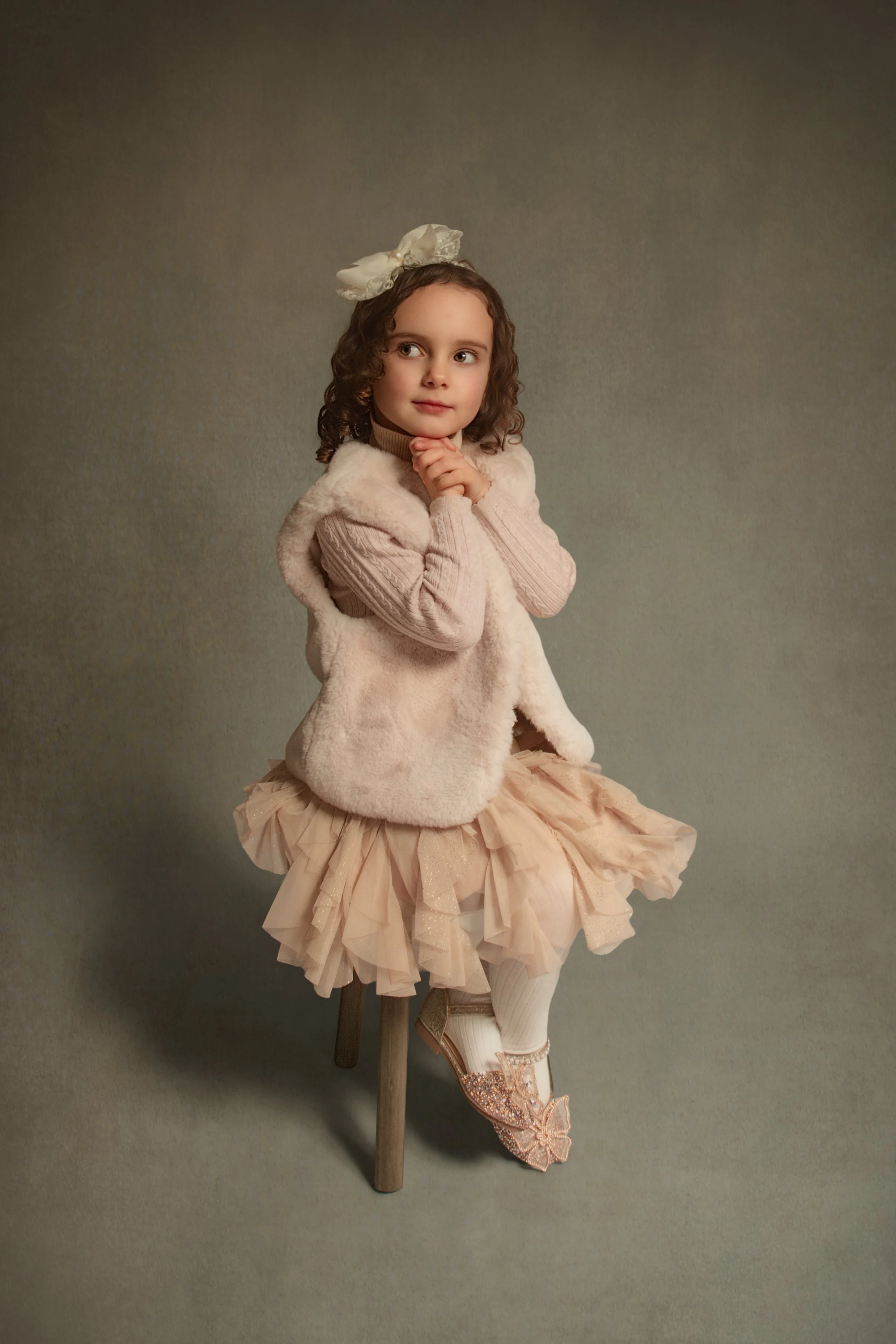 Little girl with curly brown hair sat on a stool in a fine art portrait photograph style by Manchester child and family portrait photographer