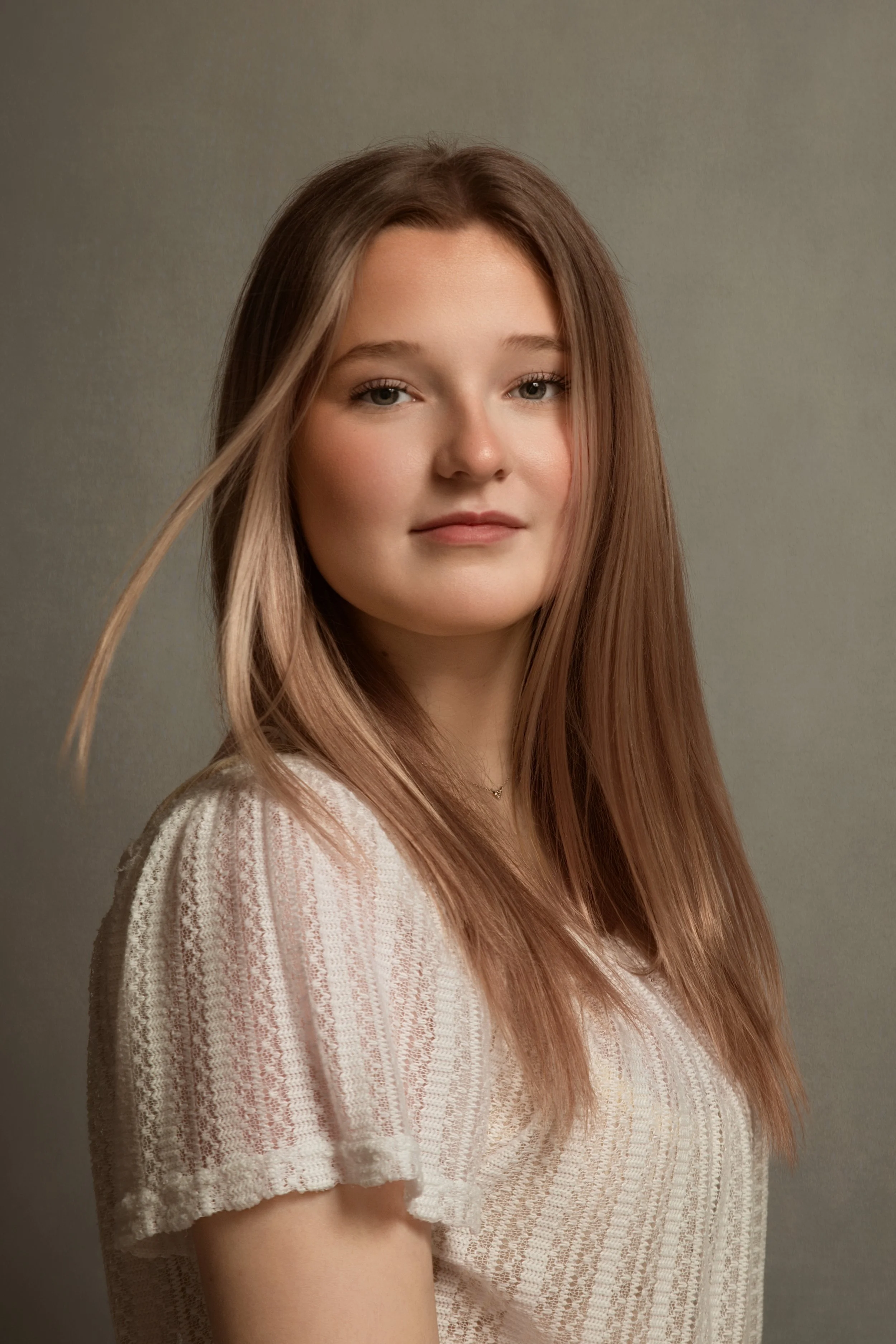 stunning photograph of a young lady with warm tones on a light background and hair blowing softly in Bury