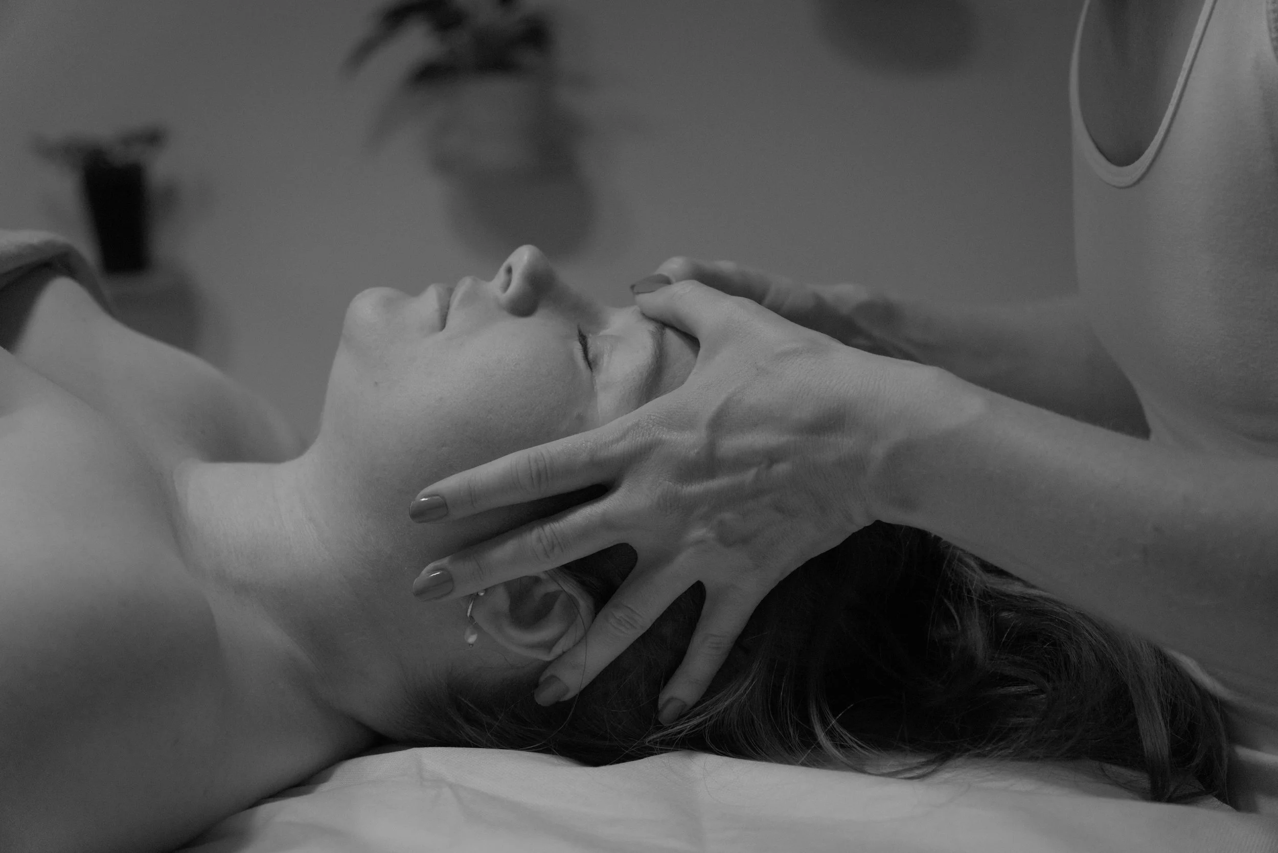 Ein Mann liegt entspannt auf einer Behandlungsliege, während eine weibliche Therapeutin eine Massage an seinem Gesicht durchführt.