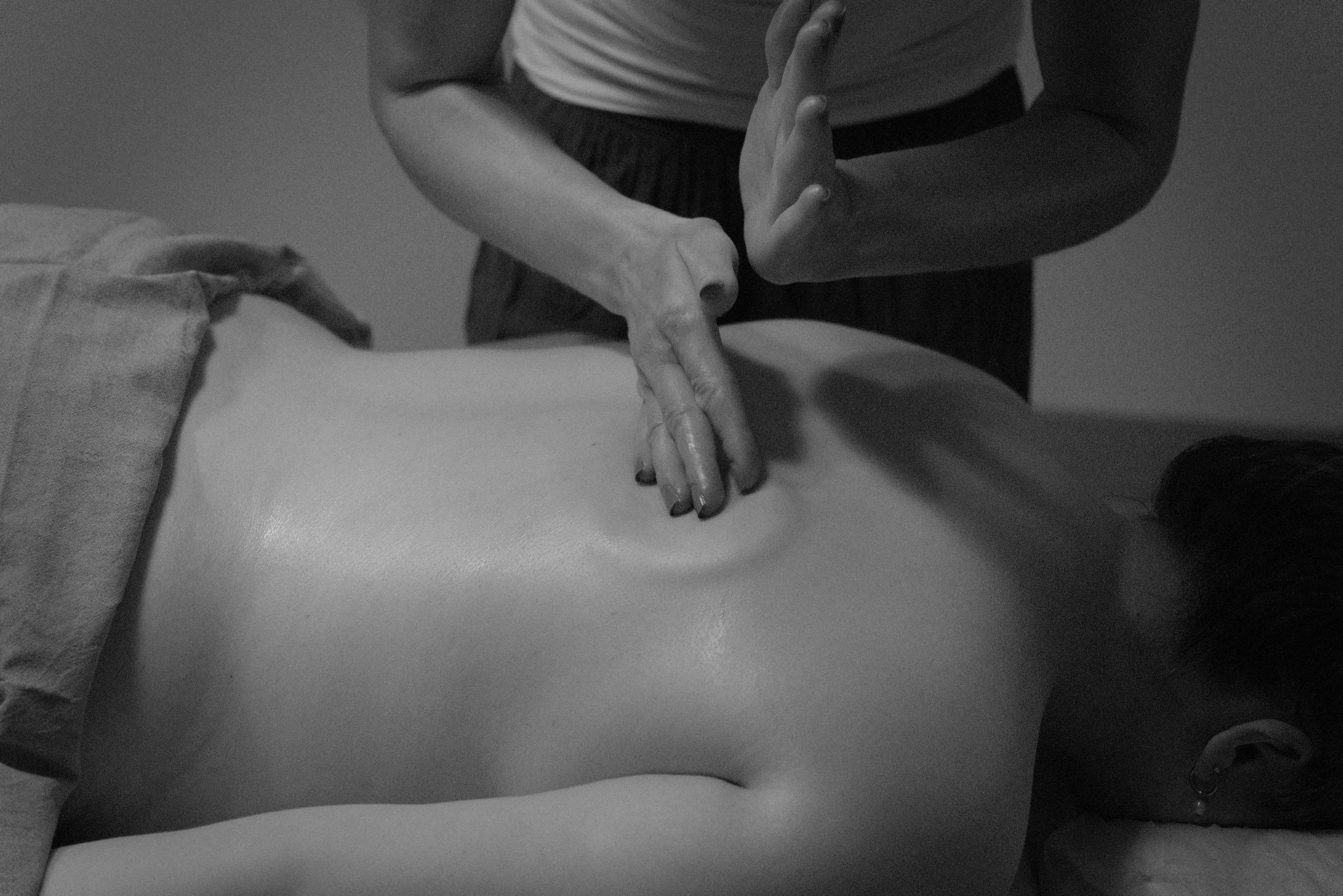 Eine Person erhält eine Rückenmassage, liegend auf einer Behandlungsliege, getragen eines grauen Sport-BH.