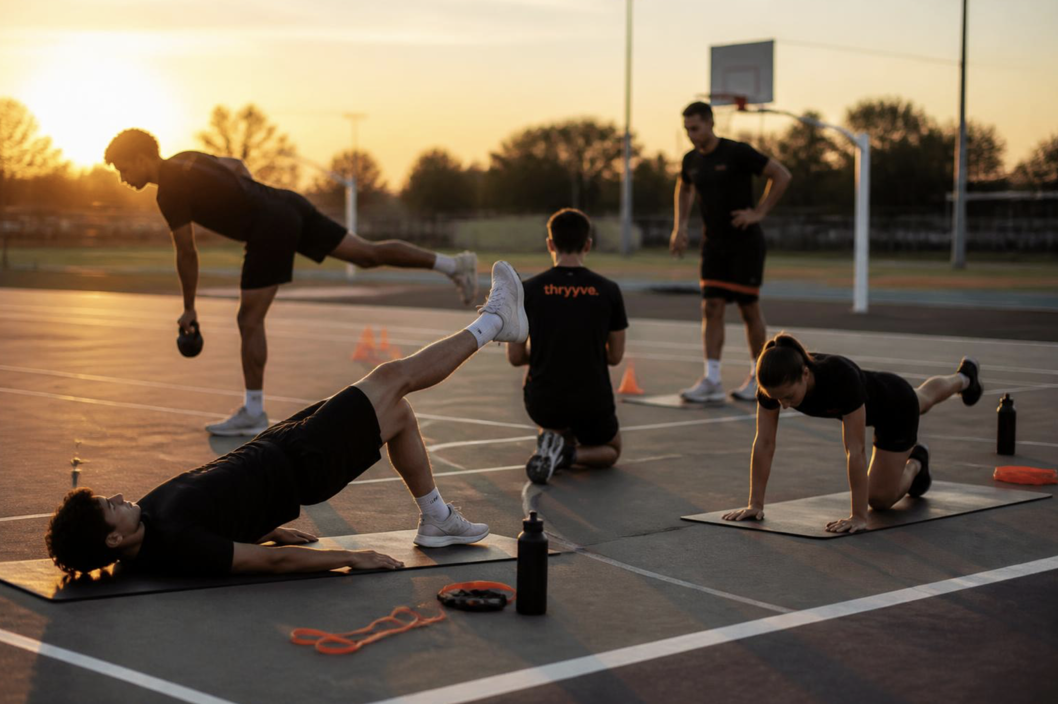 Jugendliche trainieren auf einem leeren Basketballfeld bei Sonnenuntergang, machen Übungen und Strecken im Freien.
