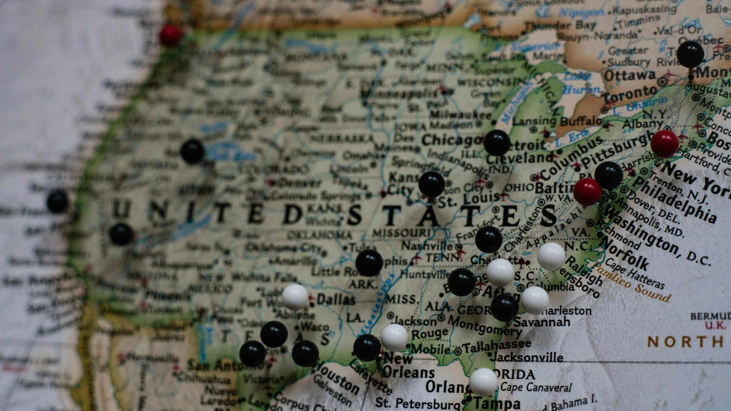 Close-up of a map of the United States with several colored pushpins marking different cities.