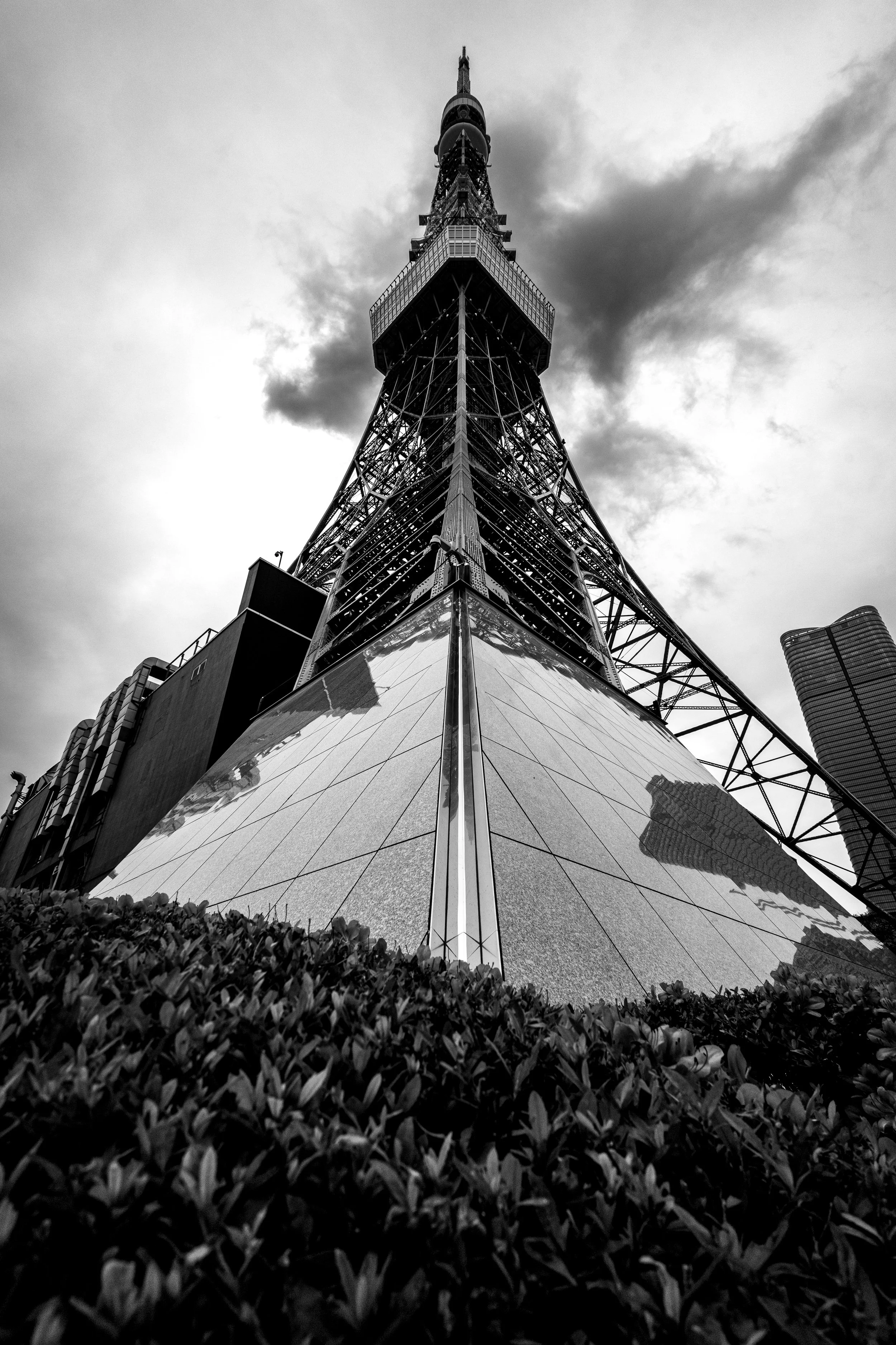 Black and white photo of Tokyo Tower, viewed from below, showing the steel structure and surrounding buildings.
