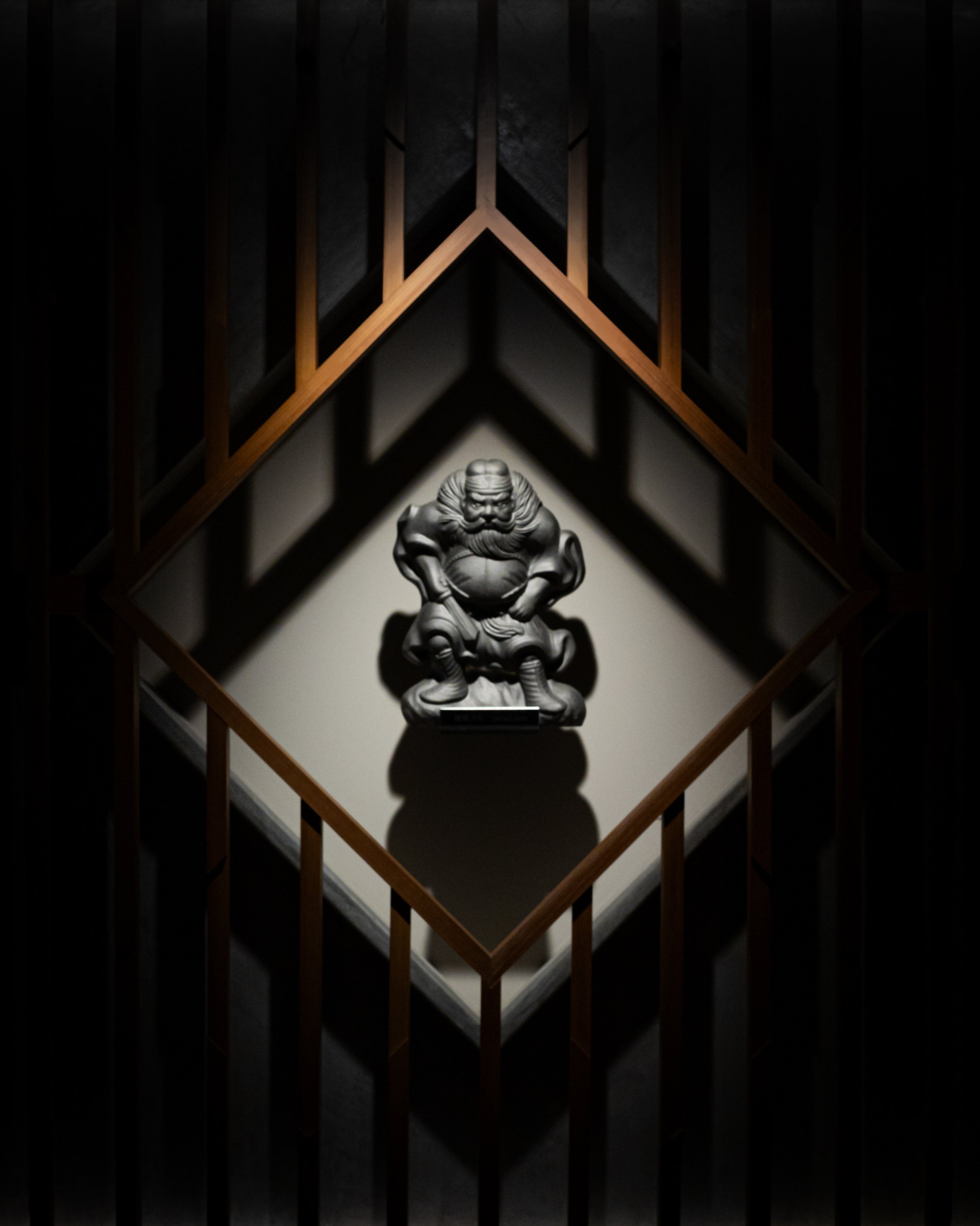 A sculpture of a mythical creature displayed on a pedestal, viewed through wooden railings in a dimly lit room.