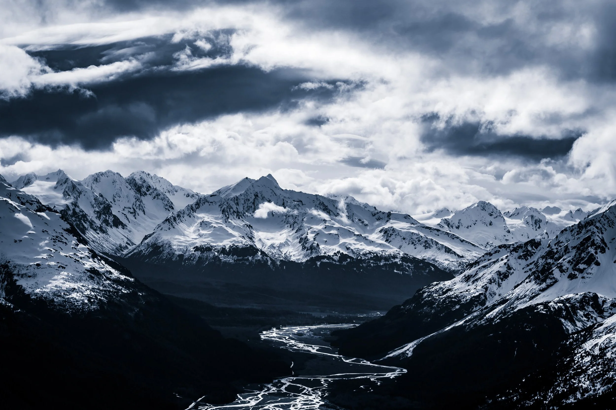Snow-covered mountains under a cloudy sky with a winding river in the valley below.