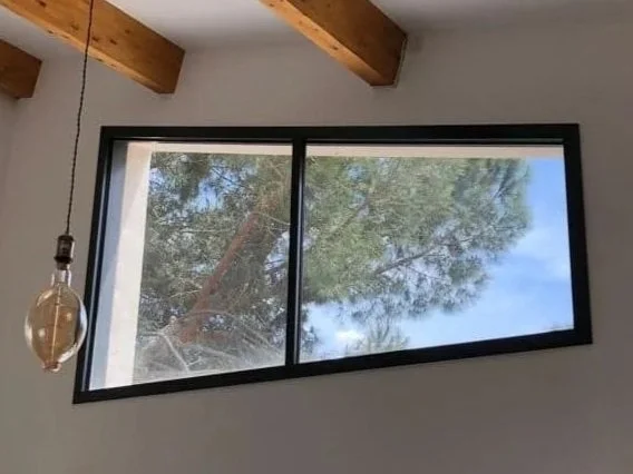 Vue au ras du sol d'une porte moustiquaire en métal avec un sol en marbre, à l'extérieur on voit des arbres verts et un ciel bleu.