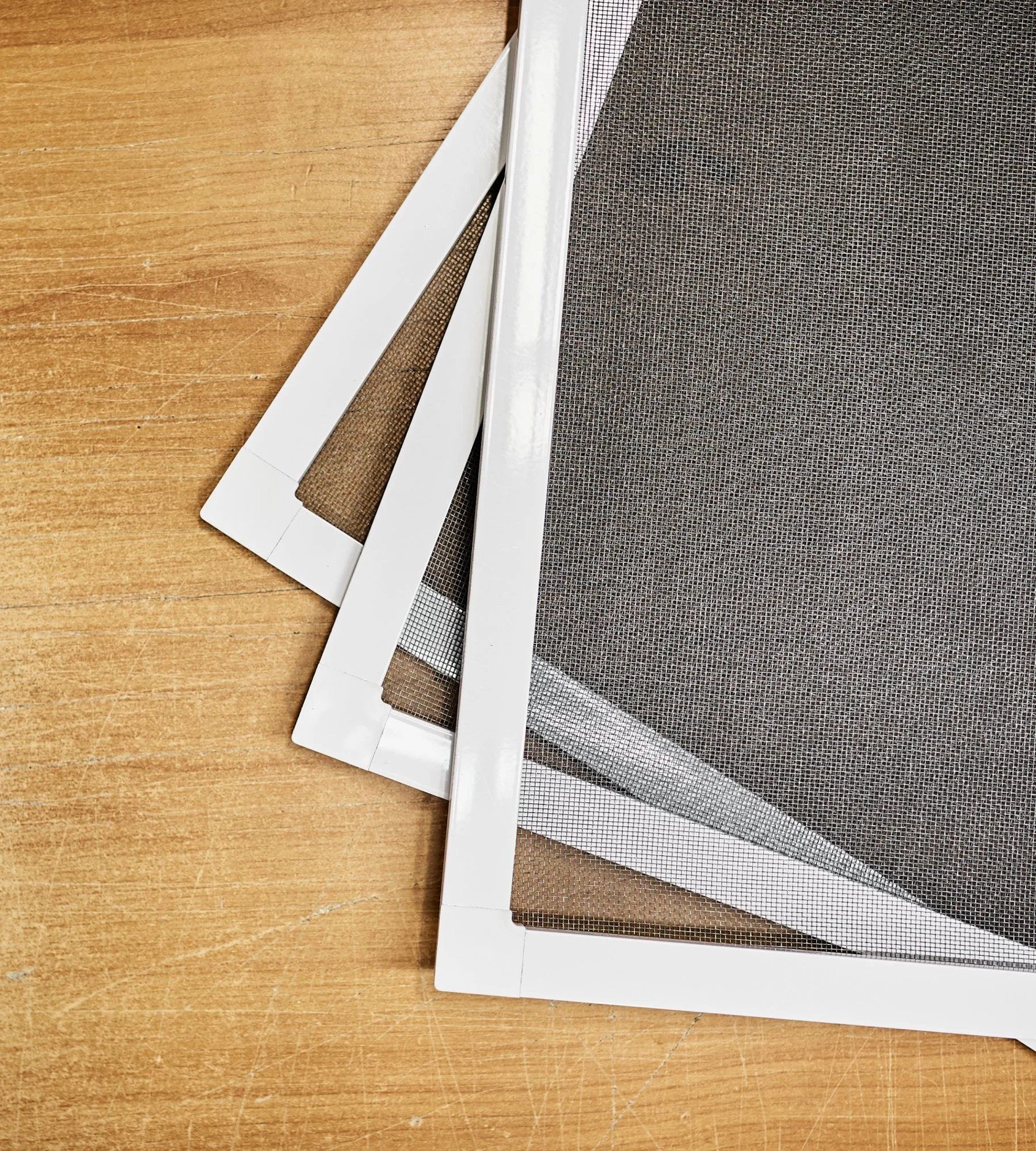 Trois cadres de moustiquaire empilés sur une surface en bois.