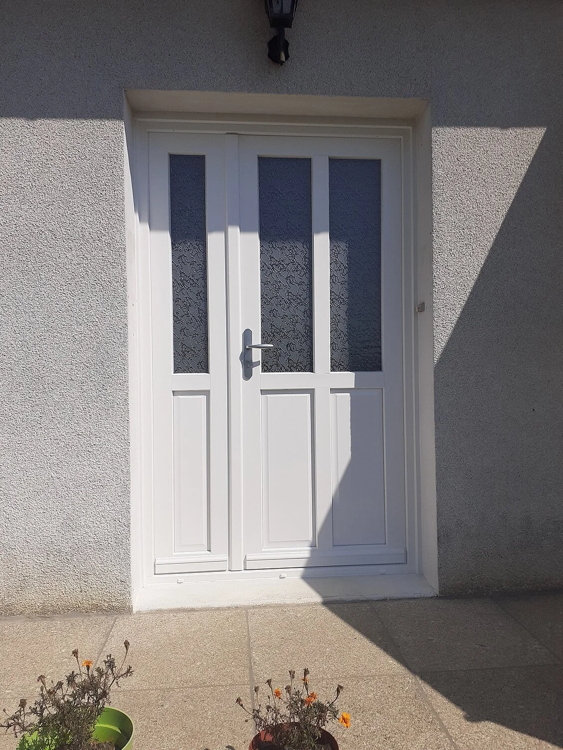 Vue au ras du sol d'une porte moustiquaire en métal avec un sol en marbre, à l'extérieur on voit des arbres verts et un ciel bleu.