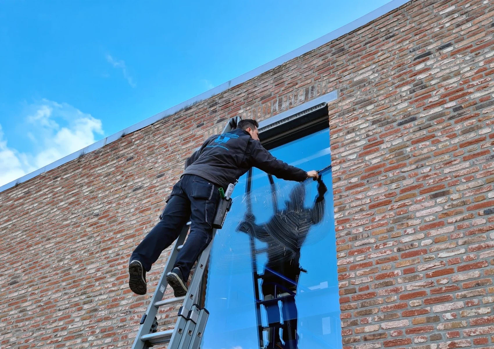 Een man staat op een ladder en reinigt de vensters van een gebouw.