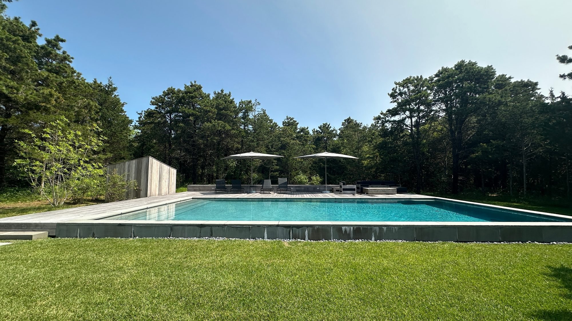 Long pool set in a green lawn ringed by pines at a modern home in Katama, Edgartown