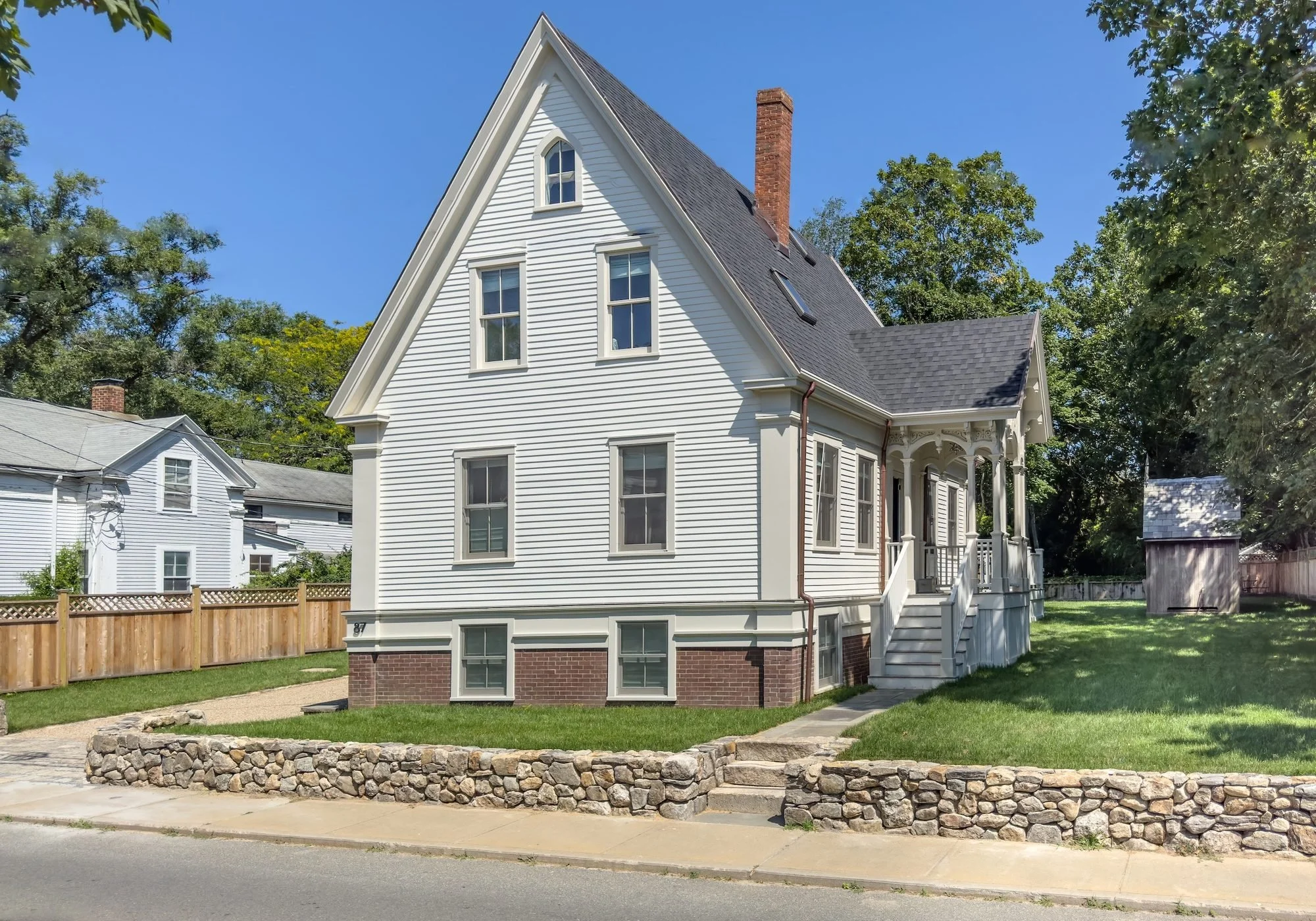 White Victorian home with a steep gable, ornate side porch and fieldstone wall in Vineyard Haven