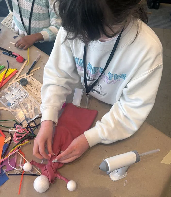 A person working on a craft project at a table with various tools and materials, including a syringe, foam balls, and fabric.